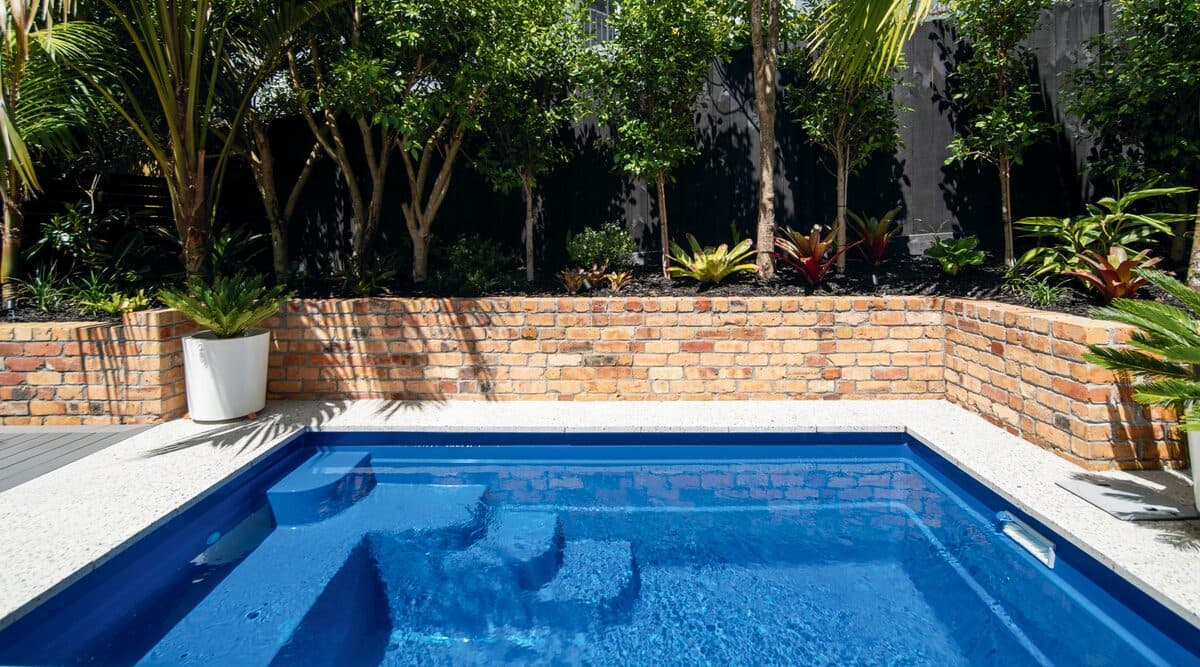 A Kiwi Urban 4 plunge pool in front of a brick garden wall