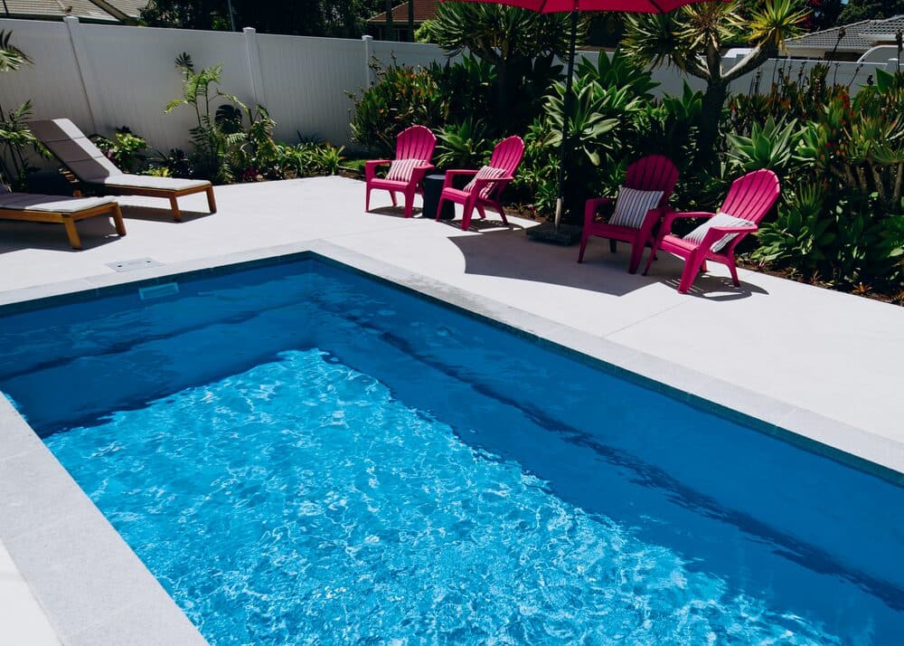 A Kiwi Dream 8 pool with pink chairs on the paving and tropical planting