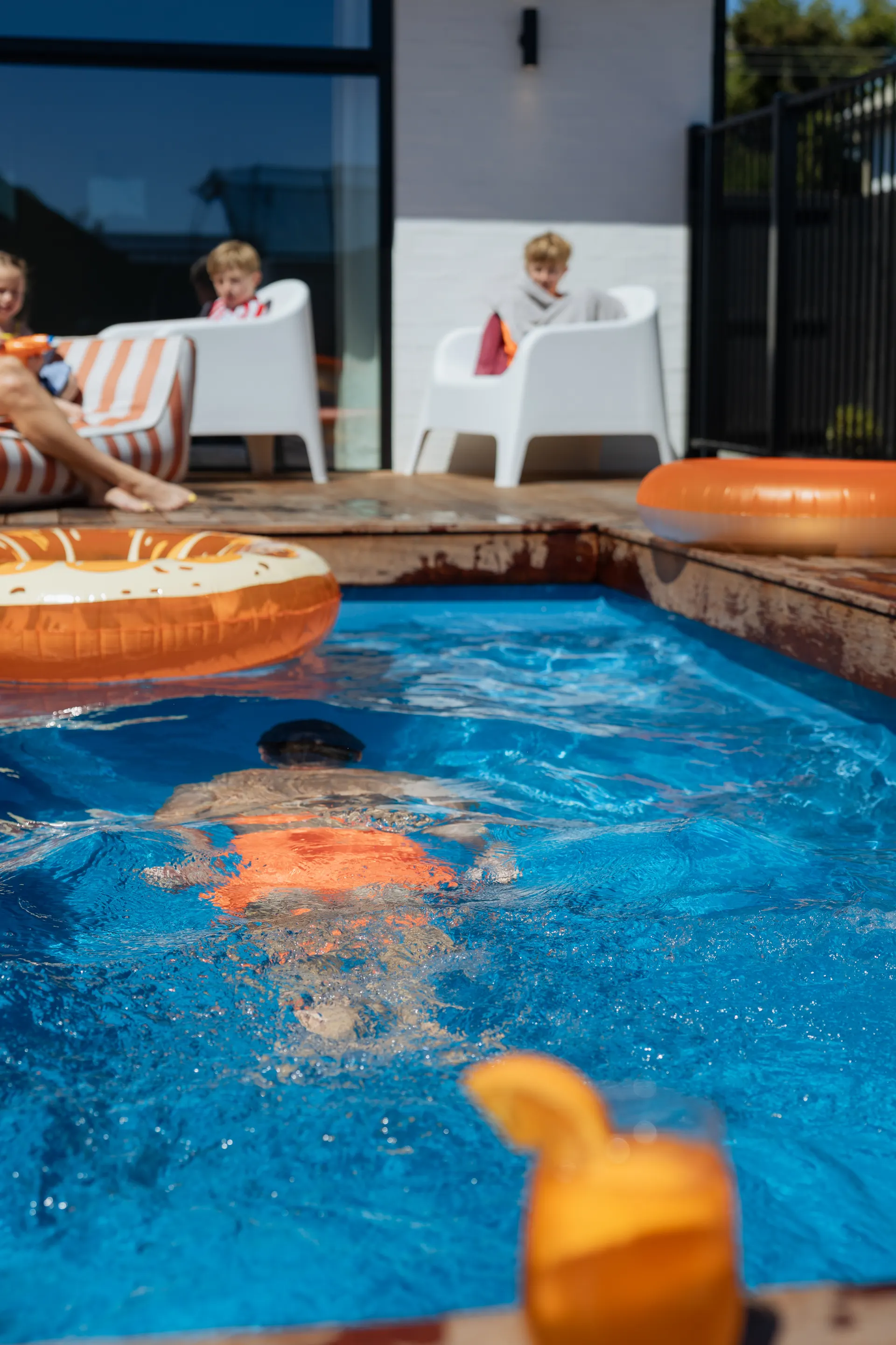 A boy swims underwater across a fibreglass pool while his family relax on the deck behind