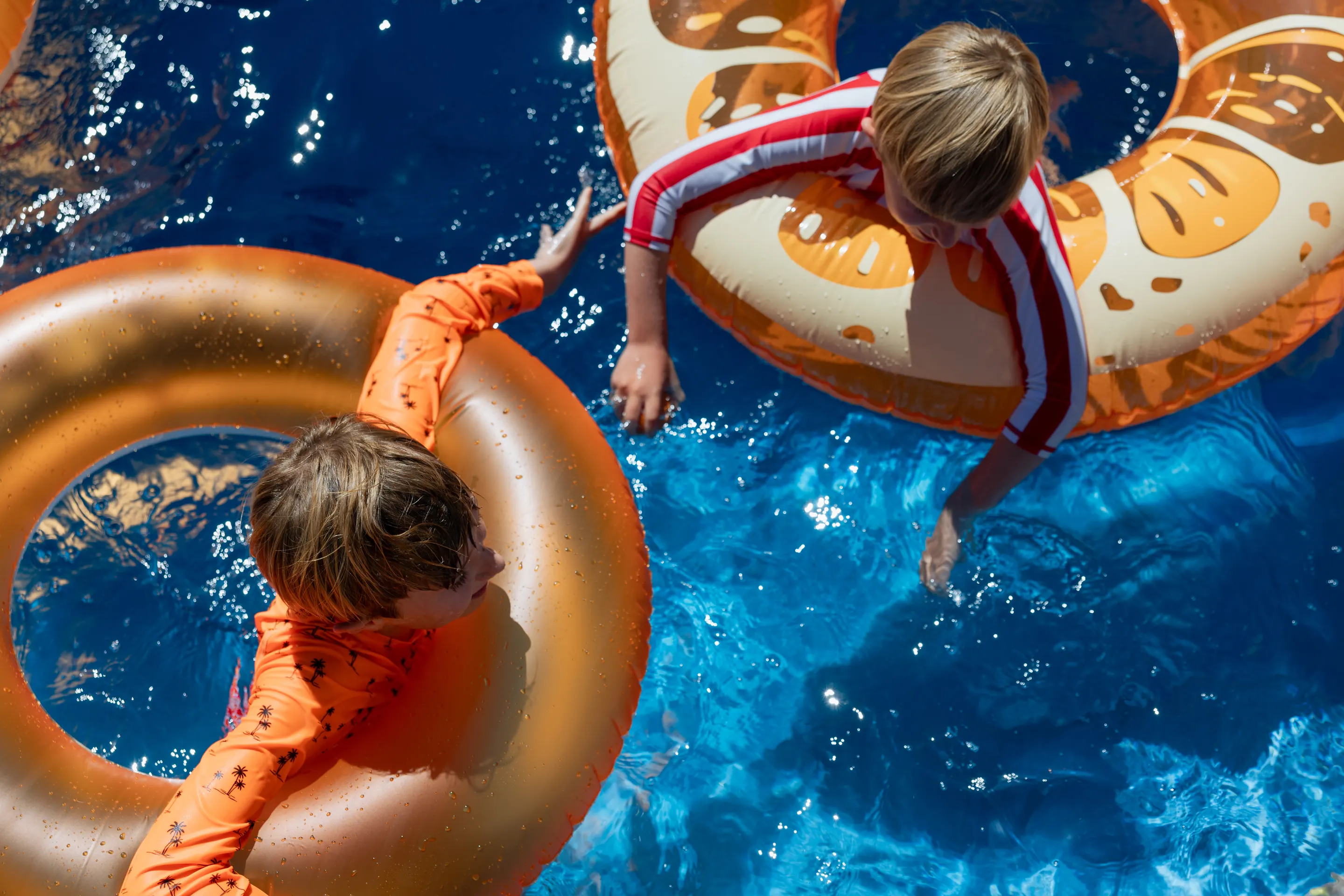 Two children float in orange pool rings in clear blue water