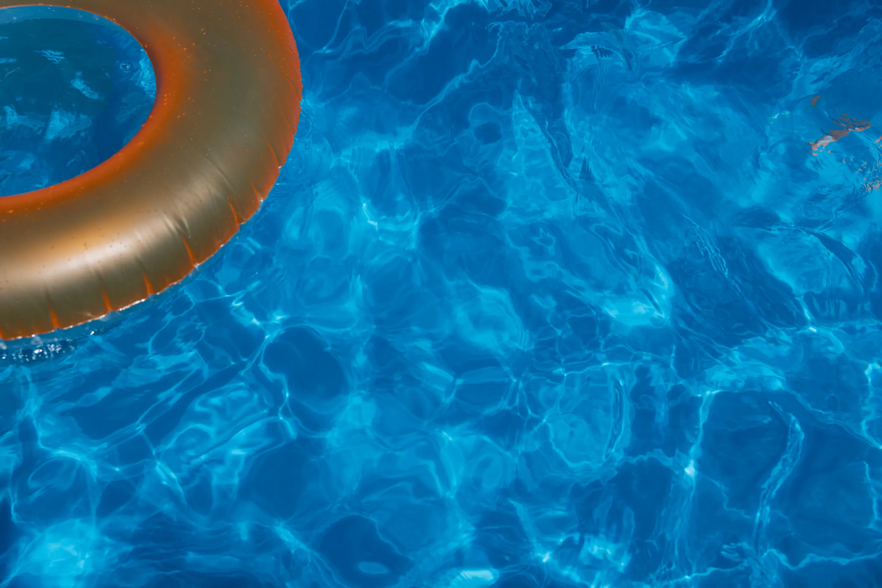 An orange pool ring floats on clear blue pool water